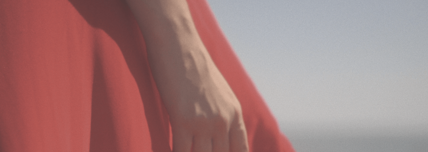 A photo by Elia Pellegrini of a woman wearing a red dress walking through a field. You can only see her from the waist down as her dress billows out in a breeze. A red dress is the symbol of the MMIWG2S movement.