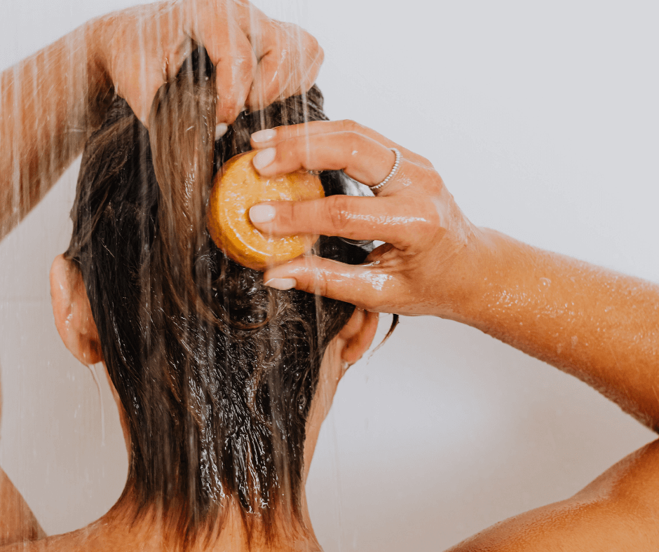 A woman takes a shower and is using a scalp scrubber.