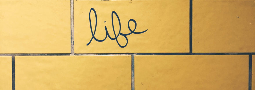 The word 'life' is written in cursive letters on a yellow shiny tile in a restroom. Photo by Tomáš Hustoles via Burst.