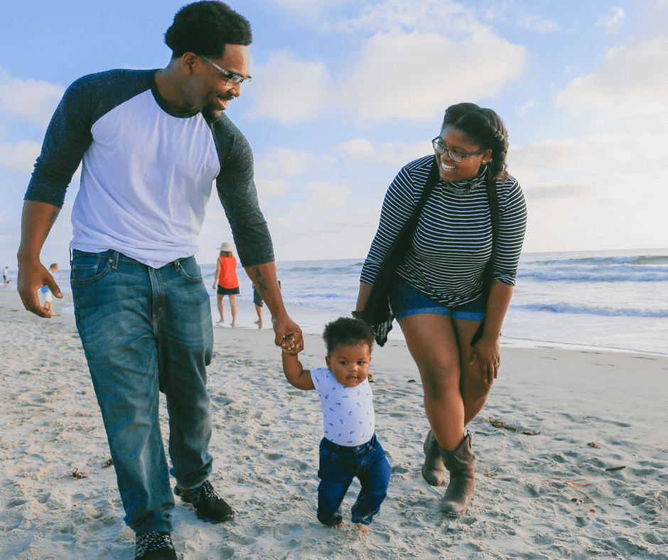 A young Black father, mother and their baby take a happy stroll on the beach. Photo by Larry Crayton via Unsplash.