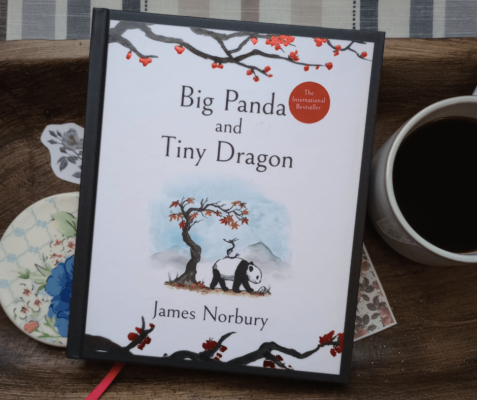 On a wooden tray next to a cup of black coffee is the book Big Panda and Tiny Dragon by James Norbury.
