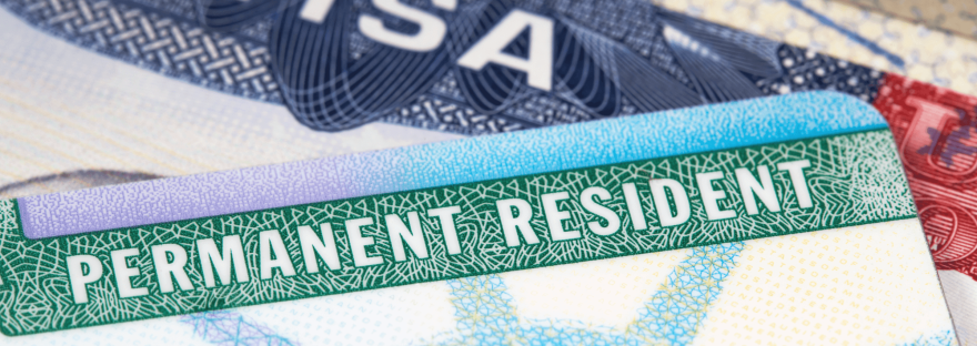 A close-up of a U.S. green card with passport visa in the background; photo via belterz/Canva.