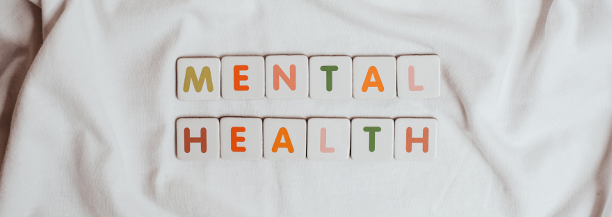 Lettered tiles that spell “mental health” laid out on a white sheet; photo via Vie Studio/Canva.