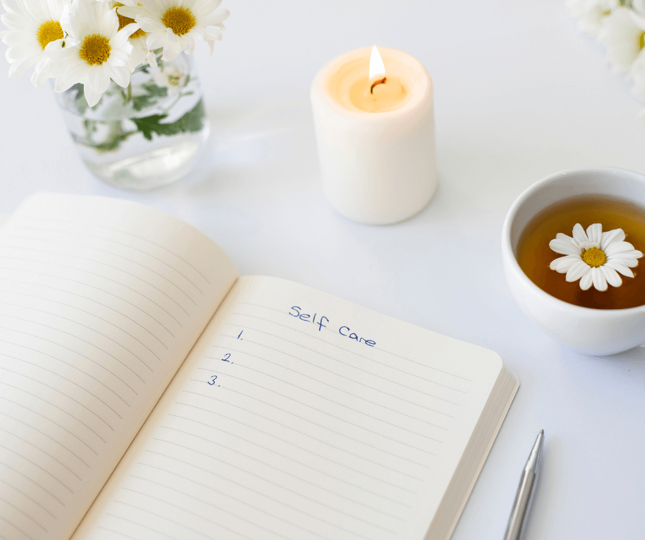 An notebook sits open on a white desk with the words, “Self-Care” written on one page.