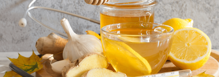 Ingredients for some home remedies (including garlic, ginger root, lemons, honey and tea) are gathered on a round wooden tray; photo via udra/Canva.